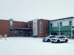 Wm. E. Hay & Stettler Elementary Remain Open Under RCMP Presence A brick and green municipal building in a snowy parking lot with two police SUVs parked in front.