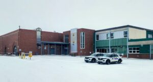 Wm. E. Hay & Stettler Elementary Remain Open Under RCMP Presence A brick and green municipal building in a snowy parking lot with two police SUVs parked in front.