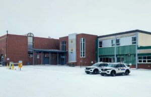 Wm. E. Hay & Stettler Elementary Remain Open Under RCMP Presence A brick and green municipal building in a snowy parking lot with two police SUVs parked in front.