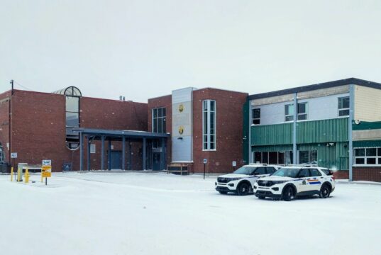 Wm. E. Hay & Stettler Elementary Remain Open Under RCMP Presence A brick and green municipal building in a snowy parking lot with two police SUVs parked in front.
