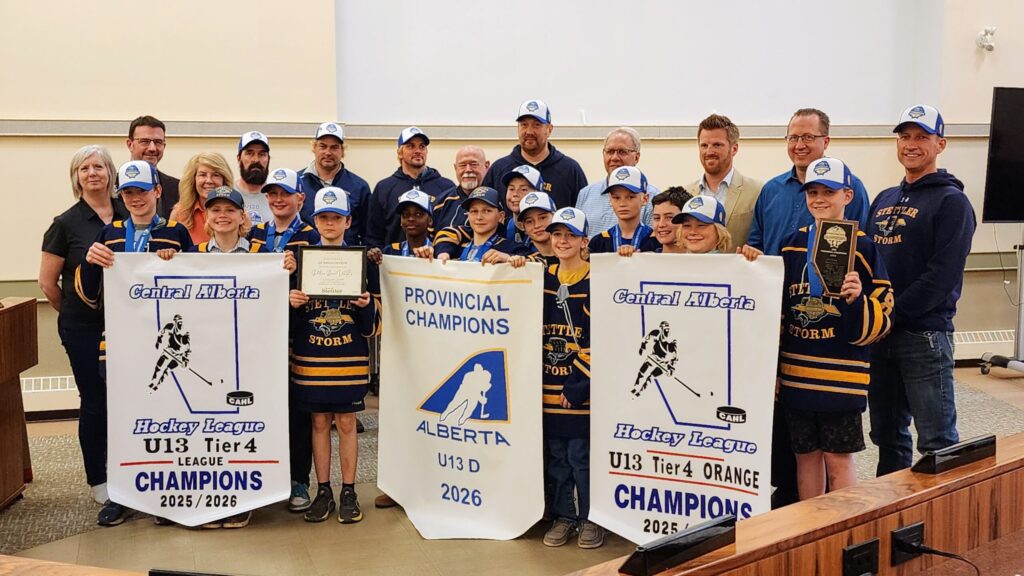 Group of kids in hockey uniforms with coaches, holding banners that read U13 Tier 4 Champions and Central Alberta Hockey League.