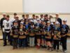 Stettler Hockey Teams Invited To Town Council To Celebrate Championship Wins Group of young hockey players in navy and gold jerseys with medals, posing for a team photo with a large trophy and certificate; coaches stand behind them in an indoor venue.