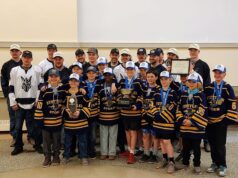 Stettler Hockey Teams Invited To Town Council To Celebrate Championship Wins Group of young hockey players in navy and gold jerseys with medals, posing for a team photo with a large trophy and certificate; coaches stand behind them in an indoor venue.