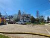Stettler Fire Department Responds To House Fire Across From School Complex Firefighters connect a large hose to a fire truck in a suburban intersection on a sunny day, with a white house nearby.
