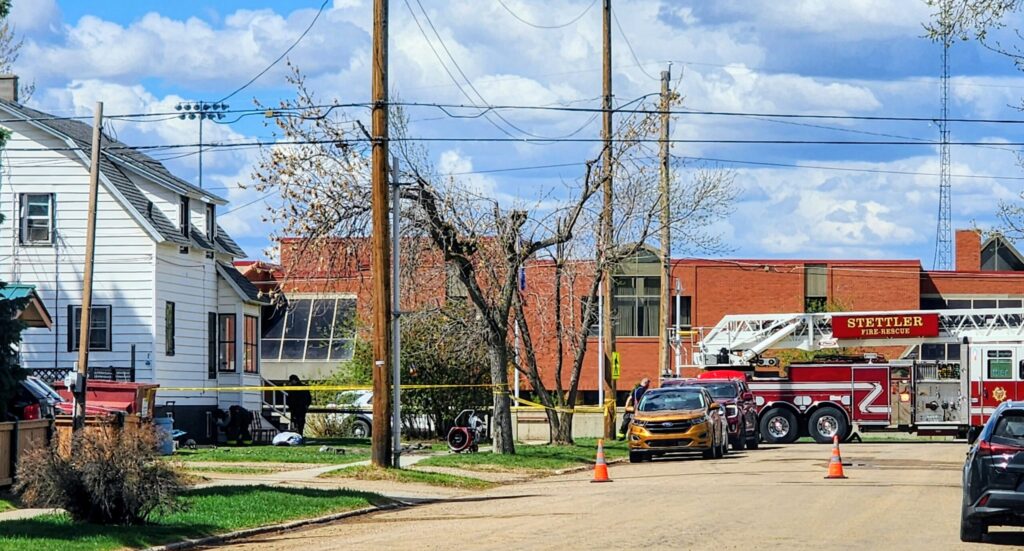 Fire truck with an extended ladder on a residential street, yellow tape cordoning off the area and orange traffic cones nearby.