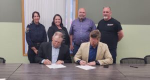 Town of Stettler & County of Stettler Declare May 25-29 As Alberta Rural Health Week Two men seated at a long table sign documents while four colleagues stand behind them in a meeting room.