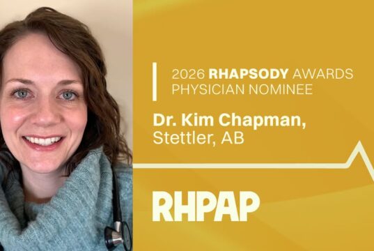 Stettler Physician & Ambulance Team Nominated For RHPAP Awards Portrait of a smiling female physician with a stethoscope, set against a gold panel that reads '2026 RHAPSODY AWARDS PHYSICIAN NOMINEE' on the right side.