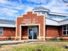 Stettler County Scales Back Buffalo Lake Upgrade Plans For 2026 Brick county office building with a stepped brick facade and glass entrance doors, blue sky above, and a small grassy area in front.