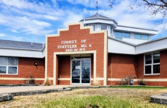 County of Stettler Ends Intermunicipal Agreements with Kneehill, Red Deer, Lacombe Counties Brick county office building with a stepped brick facade and glass entrance doors, blue sky above, and a small grassy area in front.