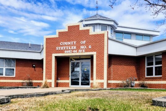 Stettler County Awards Contract For Boehlke’s Pond Revitalization Study Brick county office building with a stepped brick facade and glass entrance doors, blue sky above, and a small grassy area in front.