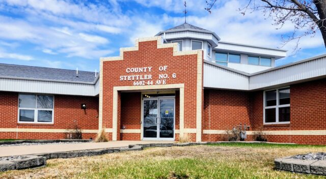 Brick county office building with a stepped brick facade and glass entrance doors, blue sky above, and a small grassy area in front.