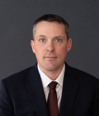Drumheller-Stettler UCP MLA Nate Horner Not Seeking Re-Election Professional headshot of a man in a navy suit and burgundy tie against a dark gray background.