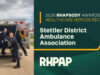 Stettler District Ambulance Association Awarded 2026 Rhapsody Healthcare Heroes Award Five paramedics pose in front of an open ambulance, celebrating a healthcare heroes award ceremony on a sunny day.