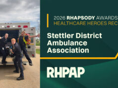 Stettler District Ambulance Association Awarded 2026 Rhapsody Healthcare Heroes Award Five paramedics pose in front of an open ambulance, celebrating a healthcare heroes award ceremony on a sunny day.