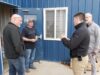 SREMA & Board of Trade Partner To Mobilize Local Business For Disaster Response Four men stand outside a blue metal building, casually chatting near a window and door.