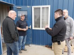 SREMA & Board of Trade Partner To Mobilize Local Business For Disaster Response Four men stand outside a blue metal building, casually chatting near a window and door.
