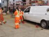 Stettler Young Women in Trades Workshop Gives Students Hands-On Experience Group of workers in high-visibility orange suits standing around a white van on jack stands in a workshop fallow area with shelves in the background.