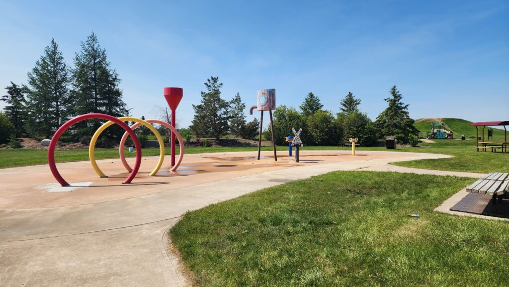 Colorful looping arches in a playground on a sunny day with trees and a grassy park in the background.