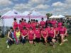 Breasties In The Buff Make Impressive Debut At Edmonton Dragon Boat Festival Group of women in matching pink shirts and hats pose together at an outdoor event under white tents that say 'Breasties in the Buff' on a sunny day.