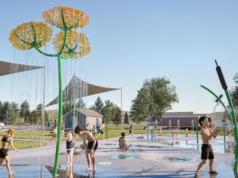 Stettler Spray Park Upgrade to Direct Recycled Water to Local Golf Course Children playing on a splash pad with yellow flower water jets under a blue sky.