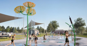 Stettler Spray Park Upgrade to Direct Recycled Water to Local Golf Course Children playing on a splash pad with yellow flower water jets under a blue sky.