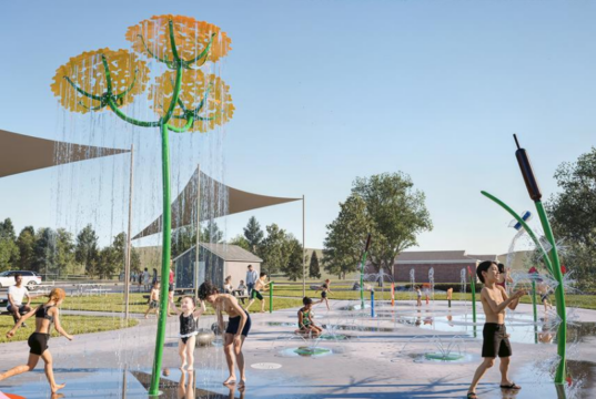Stettler Spray Park Upgrade to Direct Recycled Water to Local Golf Course Children playing on a splash pad with yellow flower water jets under a blue sky.