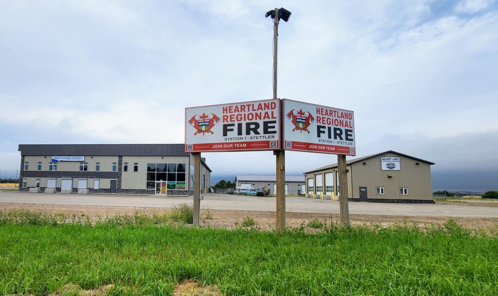 Two Heartland Regional Fire signs mounted on posts in front of a beige commercial building under a cloudy sky, with green grass in the foreground.