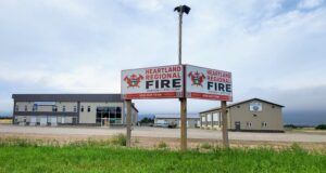 Heartland Regional Fire Downgrades Fire Restriction To Fire Advisory Two Heartland Regional Fire signs mounted on posts in front of a beige commercial building under a cloudy sky, with green grass in the foreground.