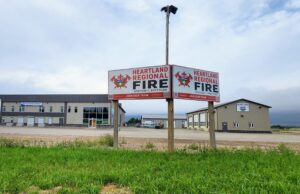 Stettler County Approves Formation of Heartland Regional Fire Commission Two Heartland Regional Fire signs mounted on posts in front of a beige commercial building under a cloudy sky, with green grass in the foreground.