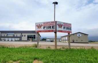 Stettler County Approves Formation of Heartland Regional Fire Commission Two Heartland Regional Fire signs mounted on posts in front of a beige commercial building under a cloudy sky, with green grass in the foreground.