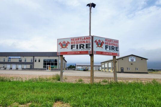 Stettler County Approves Formation of Heartland Regional Fire Commission Two Heartland Regional Fire signs mounted on posts in front of a beige commercial building under a cloudy sky, with green grass in the foreground.