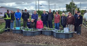 Ceremony Held For Upgraded Stettler Central Community Garden Group of diverse volunteers standing behind raised garden beds in a community garden, with houses and trees in the background.