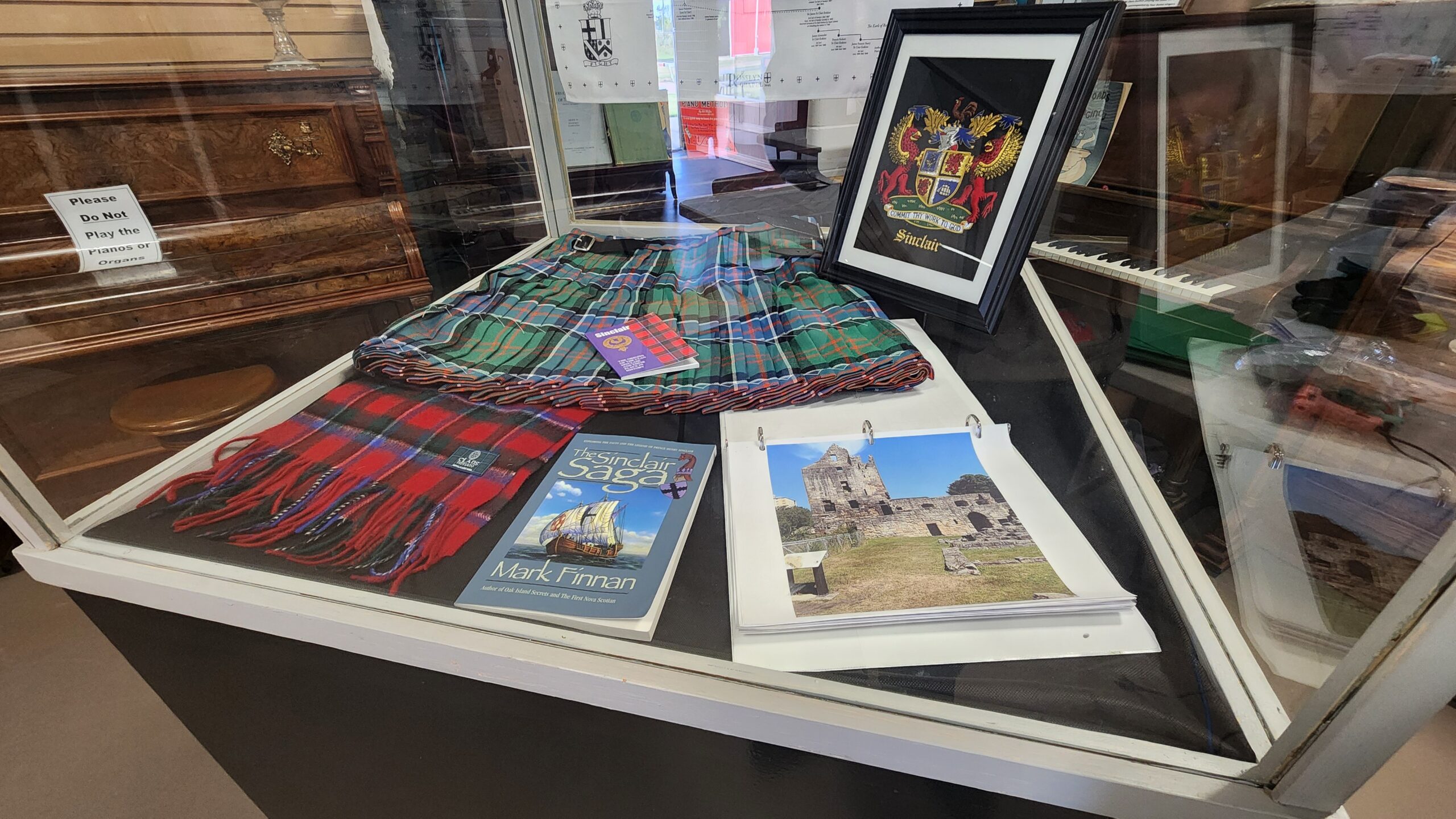 Glass display case featuring folded tartan scarves, a framed coat-of-arms poster, and travel books about Scotland.