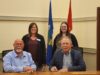 Town and County of Stettler Declare October As Pregnancy & Infant Loss Awareness Month Four adults pose in a conference room, two men seated at a table signing papers while two women stand behind them with flags in the background.