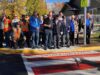 Town of Stettler and Legion Branch Dedicate Veterans Crosswalk Group photo of veterans in blazers with medals and workers in orange safety vests posing on a sidewalk in fall colors.