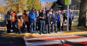 Town of Stettler and Legion Branch Dedicate Veterans Crosswalk Group photo of veterans in blazers with medals and workers in orange safety vests posing on a sidewalk in fall colors.