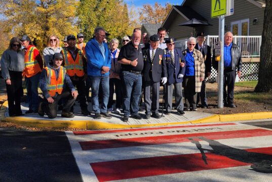 Town of Stettler and Legion Branch Dedicate Veterans Crosswalk Group photo of veterans in blazers with medals and workers in orange safety vests posing on a sidewalk in fall colors.