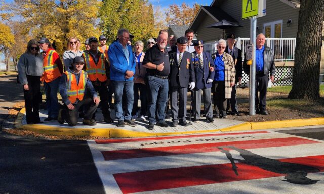20260928_110314~2 (2) Group photo of veterans in blazers with medals and workers in orange safety vests posing on a sidewalk in fall colors.