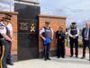 RCMP Unveil Memorial Plaque For Employees Lost To Suicide Group of uniformed officers standing in a semicircle beside a brick memorial wall with a gold-lettered plaque that reads 'Honouring the lives of RCMP employees lost to suicide' and a maple‑leaf ribbon emblem nearby.