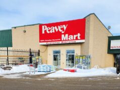 Stettler Home Hardware Moving To Vacant Peavy Mart Location In 2027 Peavey Mart storefront on a beige brick building with a large red sign, snow in the parking lot in front.