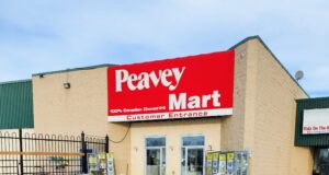 Stettler Home Hardware Moving To Vacant Peavy Mart Location In 2027 Peavey Mart storefront on a beige brick building with a large red sign, snow in the parking lot in front.