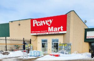 Stettler Home Hardware Moving To Vacant Peavy Mart Location In 2027 Peavey Mart storefront on a beige brick building with a large red sign, snow in the parking lot in front.