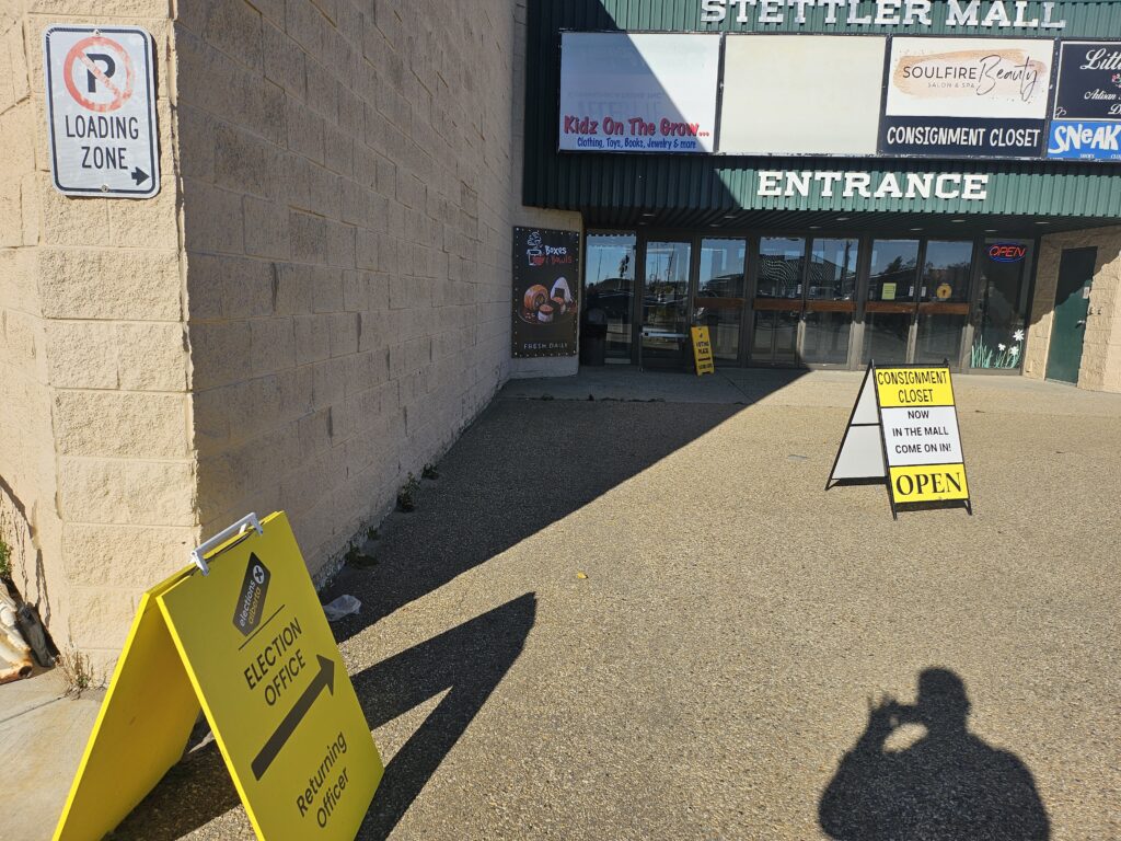 Entrance to a mall with glass doors under a green awning; storefront signs above and a beige wall-mounted 'Loading Zone' sign nearby.