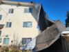 Stettler Wind Storm Tears Roof Off Apartment Building Two-story beige apartment building with a dark tarp-covered collapse in the yard against a clear blue sky.