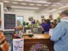 Jacked-Up Coffee Hosts Fundraiser For Stettler Resident’s Medical Expenses People line up at a cafe counter with a chalkboard menu on the left and purple streamers overhead inside a cozy shop. Behind the counter, staff prepare orders while customers wait.