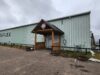2026 Remembrance Day Service Moves To Stettler Agri-Plex Green corrugated metal warehouse with a wooden entry canopy and an 'AGRIPLEX' sign on the side under a cloudy sky.