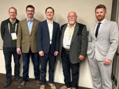 Town of Stettler Presses Province On Policing Cost Disparities At Municipal Convention Five men in business attire wearing conference badges pose together against a light wall, from left to right: casual jacket, brown blazer, navy suit, gray blazer, light gray suit.