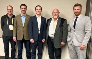 Town of Stettler Presses Province On Policing Cost Disparities At Municipal Convention Five men in business attire wearing conference badges pose together against a light wall, from left to right: casual jacket, brown blazer, navy suit, gray blazer, light gray suit.