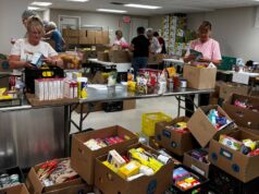 Stettler & District Food Bank Drive Raises Over $10K In Donations Volunteers sorting and packing canned goods and boxed foods at a busy food pantry workstation.