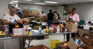 Stettler & District Food Bank Drive Raises Over $10K In Donations Volunteers sorting and packing canned goods and boxed foods at a busy food pantry workstation.